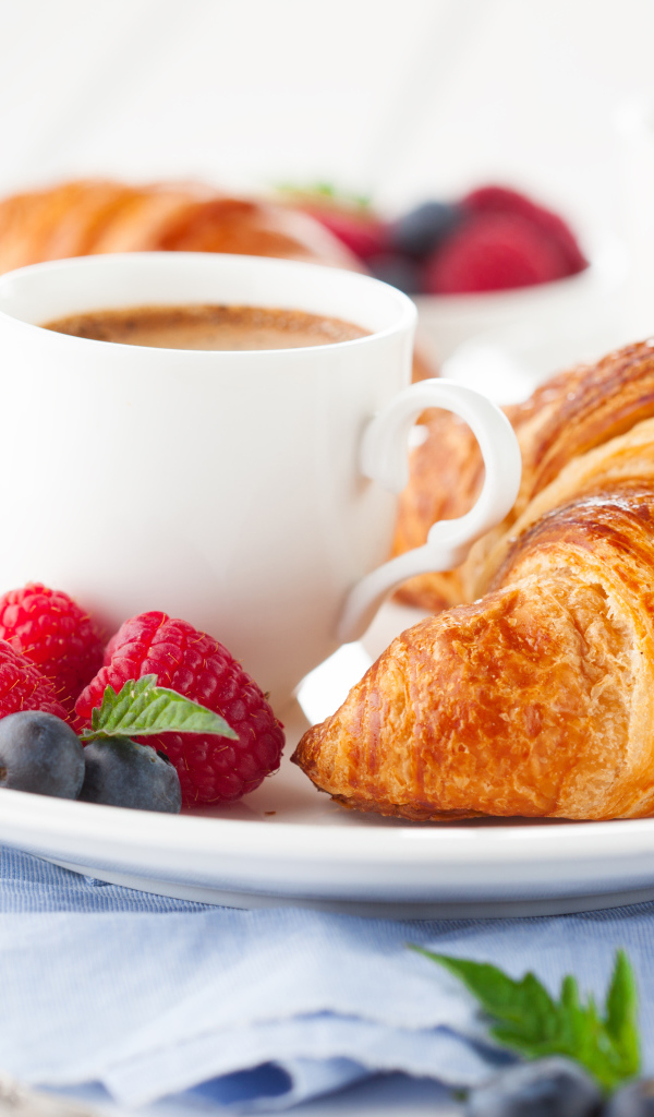 Чашка кофе на тарелке с круассаном и ягодами