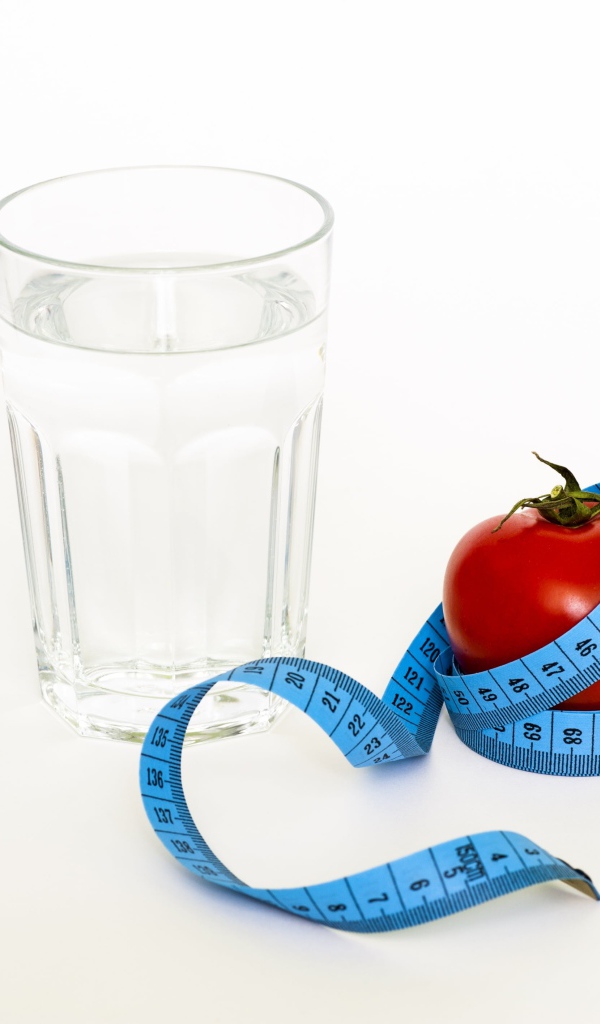 Стакан воды на белом фоне с красным помидором и сантиметром
