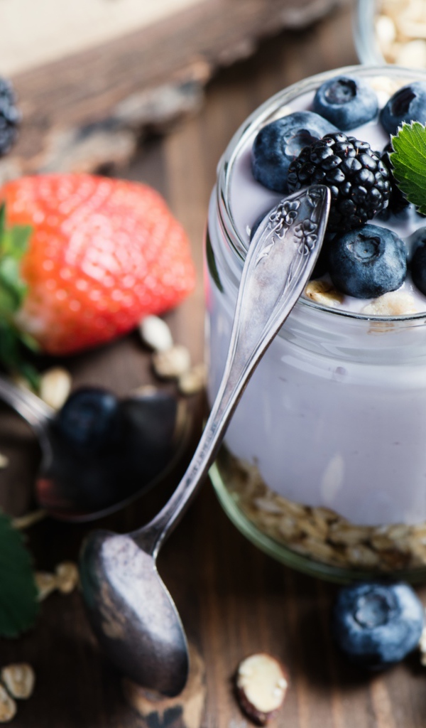 Баночка с мюсли, йогуртом и ягодами на столе с ложками