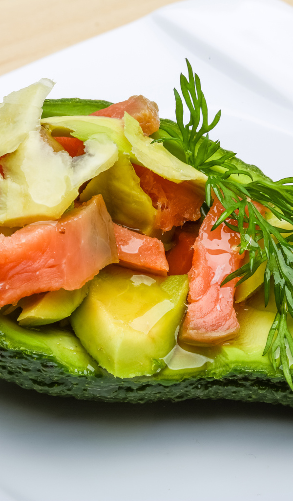 Авокадо с салатом из красной рыбы на белой тарелке