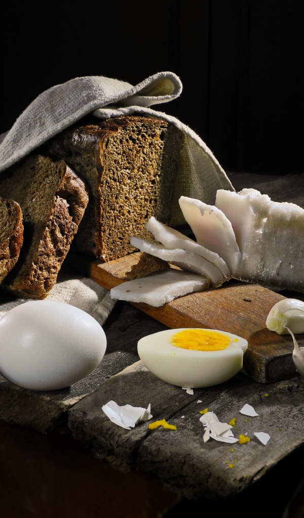 Черный хлеб, вареные яйца, чеснок и сало на деревянном столе