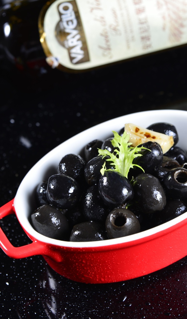 Черные оливки на столе с бутылкой и помидорами