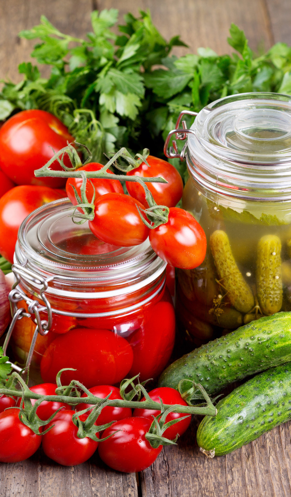 Консервированные помидоры и огурцы на столе со свежими овощами и зеленью 