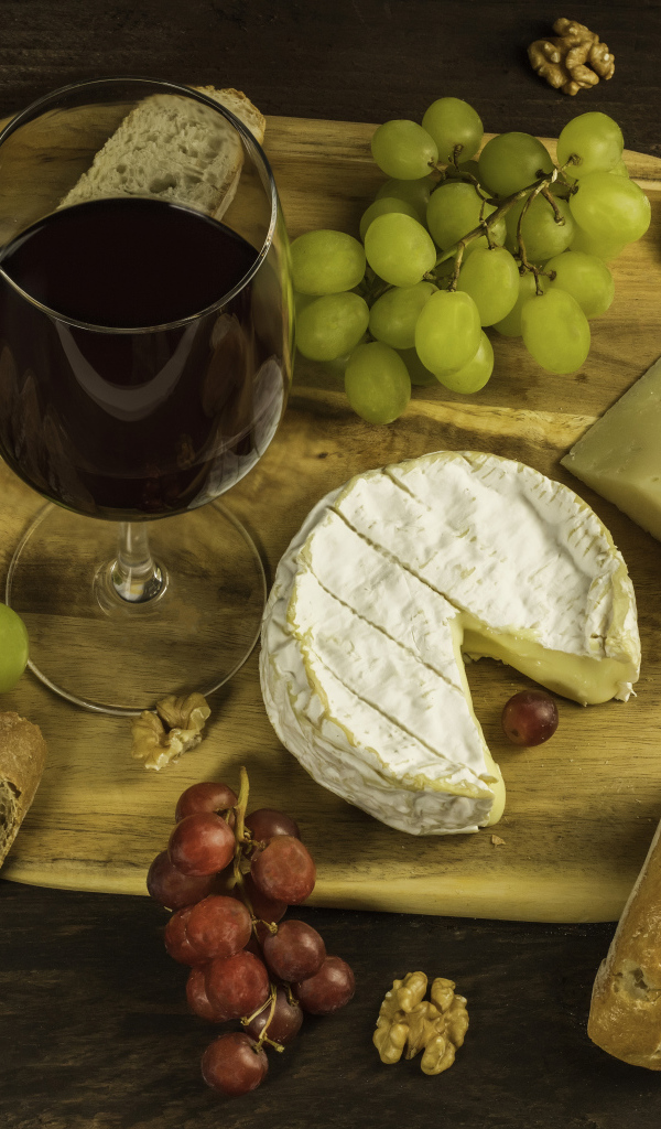Сыр на столе с орехами, хлебом, виноградом и бокалом вина