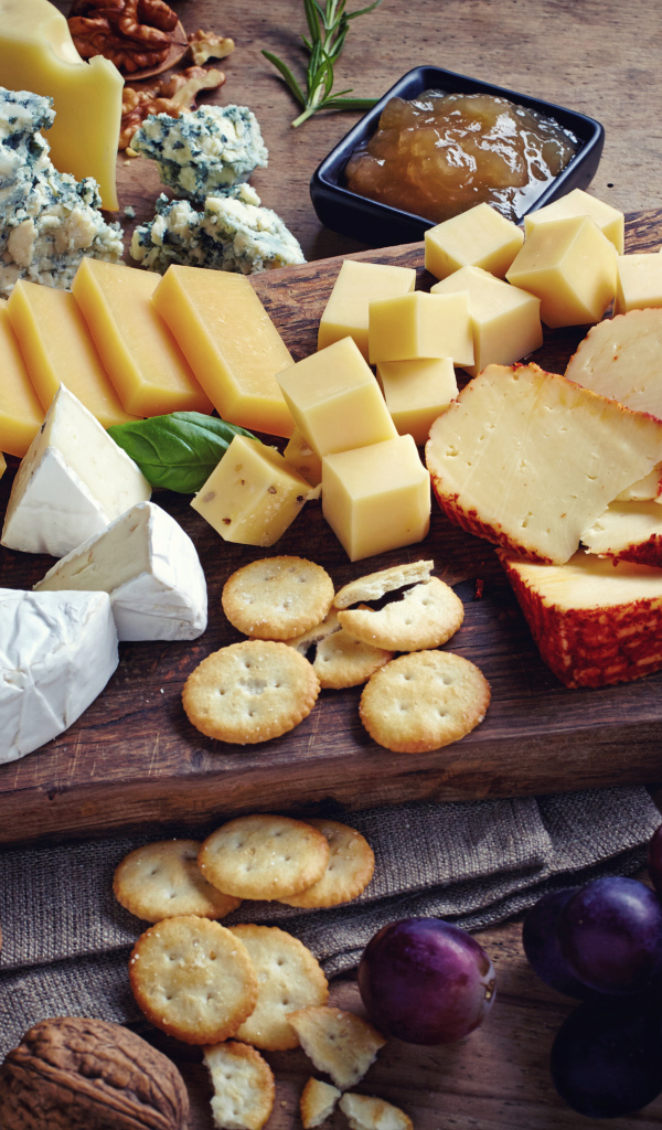 Сырная нарезка на разделочной доске на столе с виноградом и крекерами