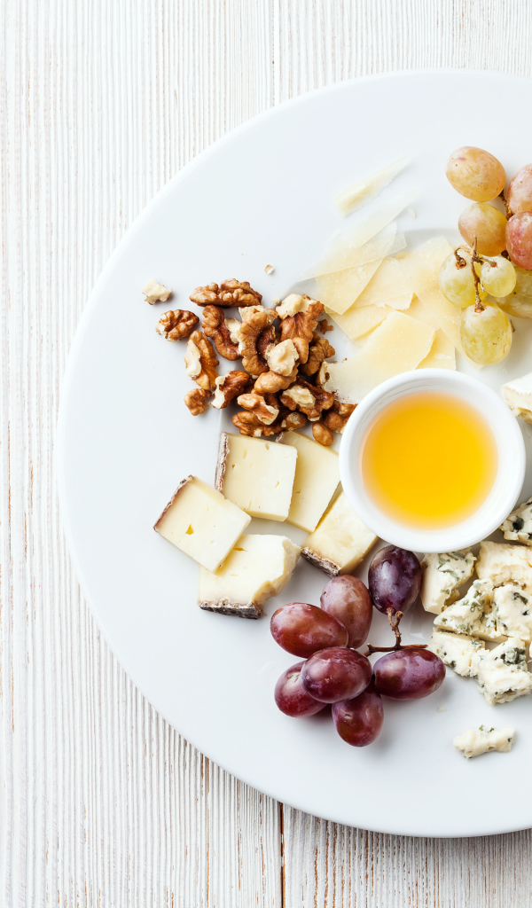 Куски сыра на тарелке с орехами, виноградом, медом и ягодами ежевики