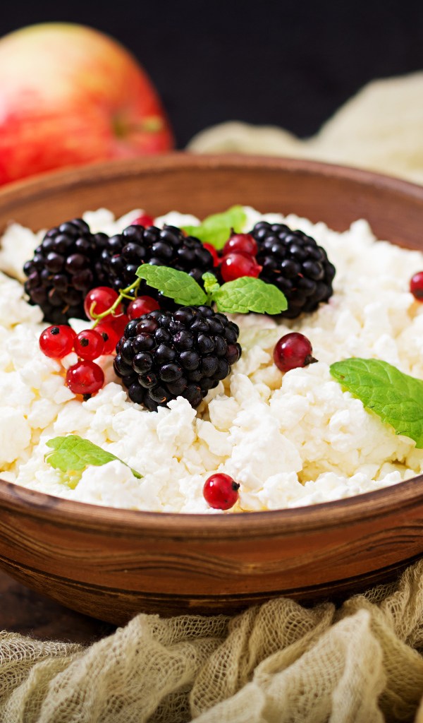 Творог с ягодами в деревянной миске на столе с яблоками