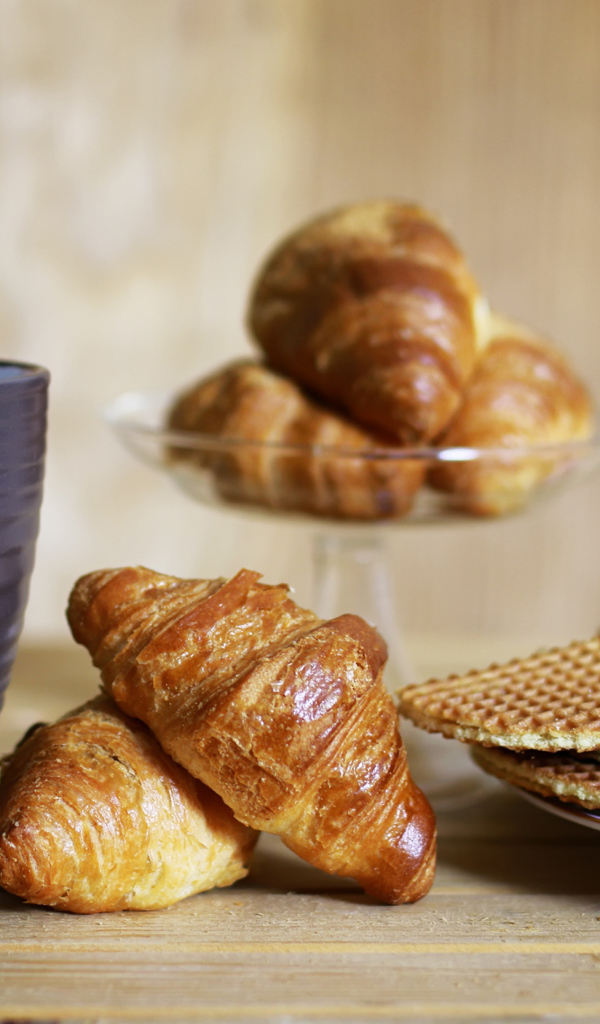 Чашка на столе с круассанами и вафлями 