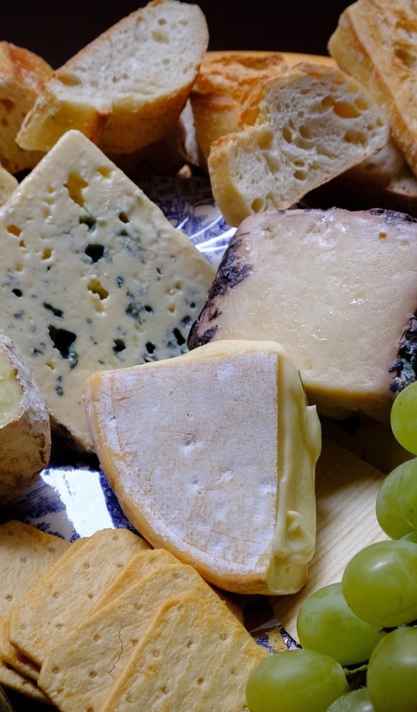 Разные виды твердого сыра на тарелке с белыми виноградом и вином