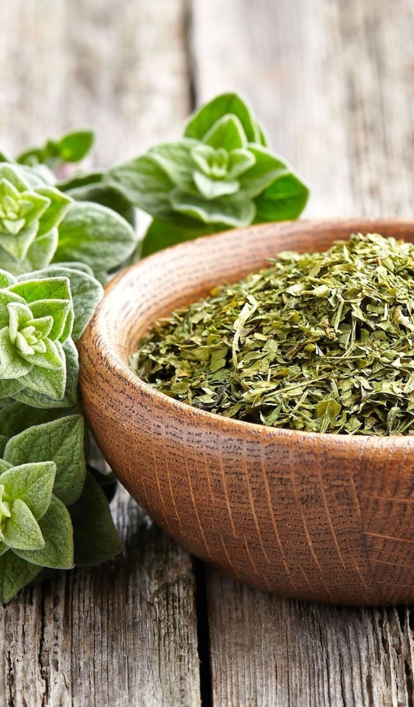 Сухая трава орегано в деревянной миске на столе 