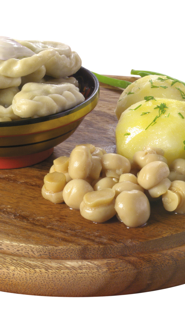 Вареники с грибами и вареной картошкой на деревянной доске на белом фоне