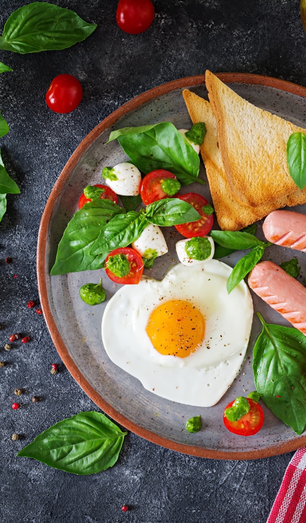 Яичница на тарелке с помидорами, гренками, сыром, сосисками и зеленью базилика