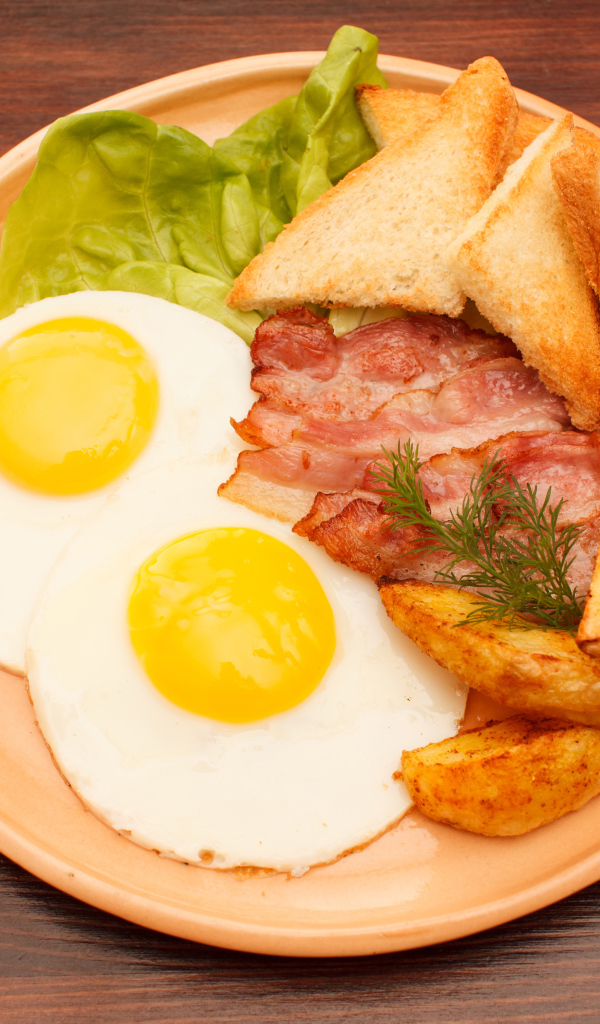 Яичница с беконом, картофелем фри и гренками на столе 