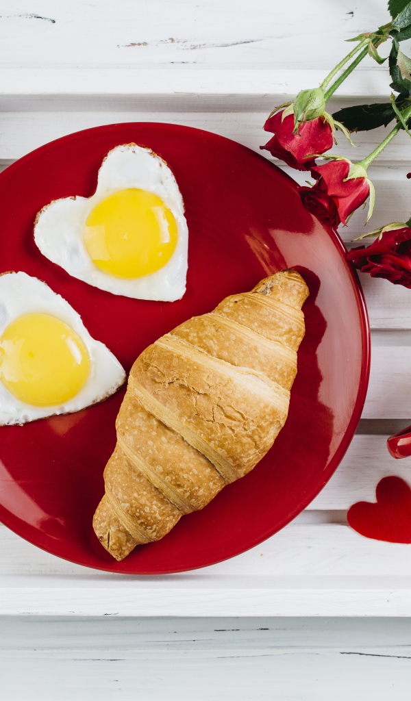 Яичница с круассаном на красной тарелке на столе букетом роз и чашкой какао