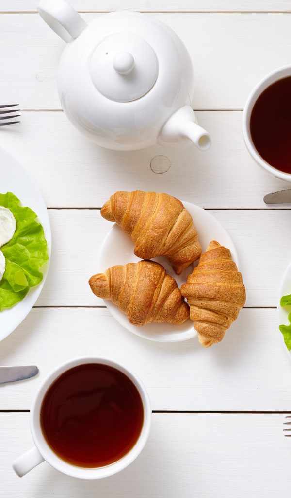 Яичница с колбасой и круассанами на столе чаем 