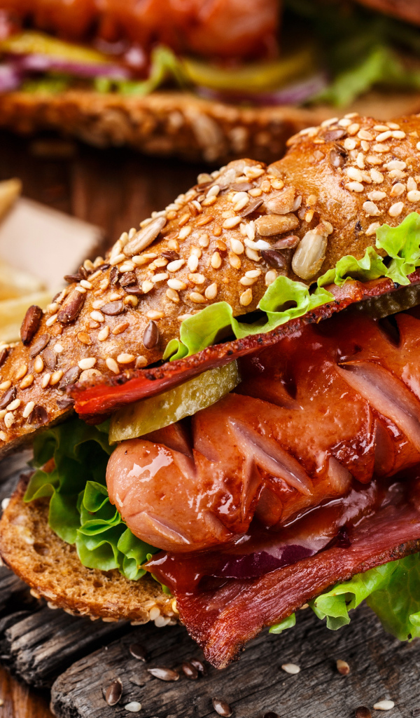 Хотдог с сосиской и беконом на столе с картофелем фри 