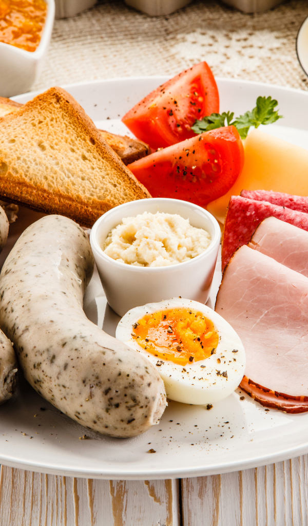 Большая белая тарелка с колбасой, яйцами, помидорами, тостами и сыром