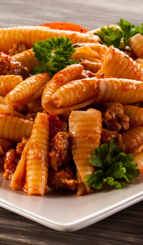 Паста с мясом, петрушкой и помидорами на белой тарелке