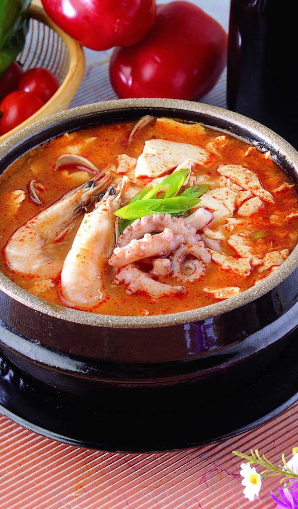 Тарелка красного супа с морепродуктами на столе с овощами 