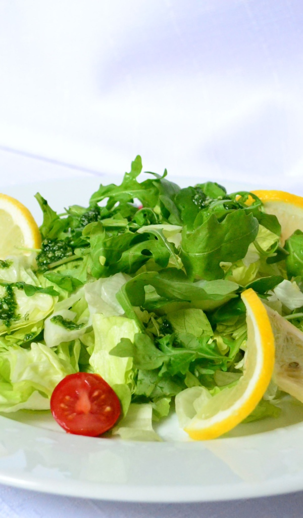 Салат с рукколой, лимоном и помидорами на белой тарелке