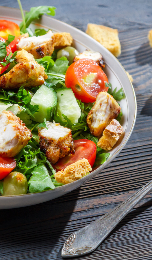 Салат с овощами, сухариками и курицей и на столе с вилкой