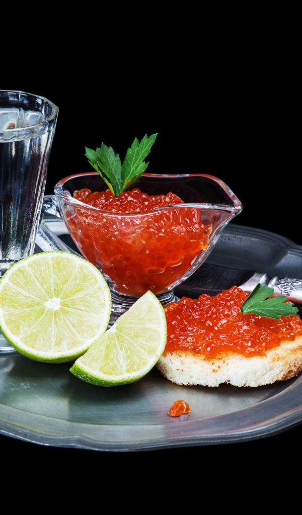 Бутерброды с красной икрой на подносе с рюмкой водки и лаймом