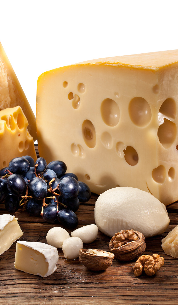 Куски сыра на деревянном столе с виноградом и грецким орехом