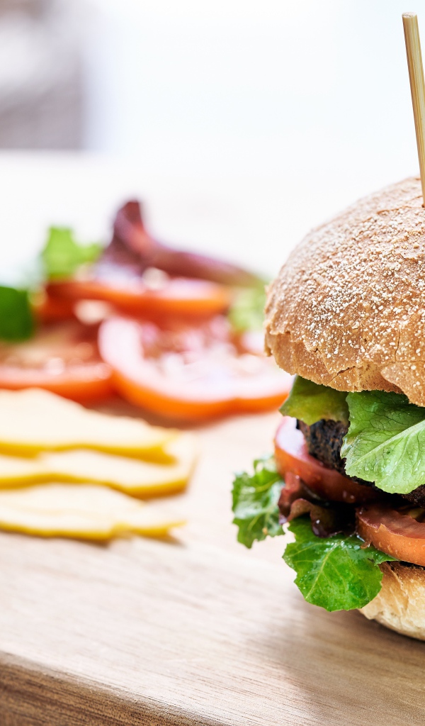 Аппетитный гамбургер на доске с сыром и помидорами