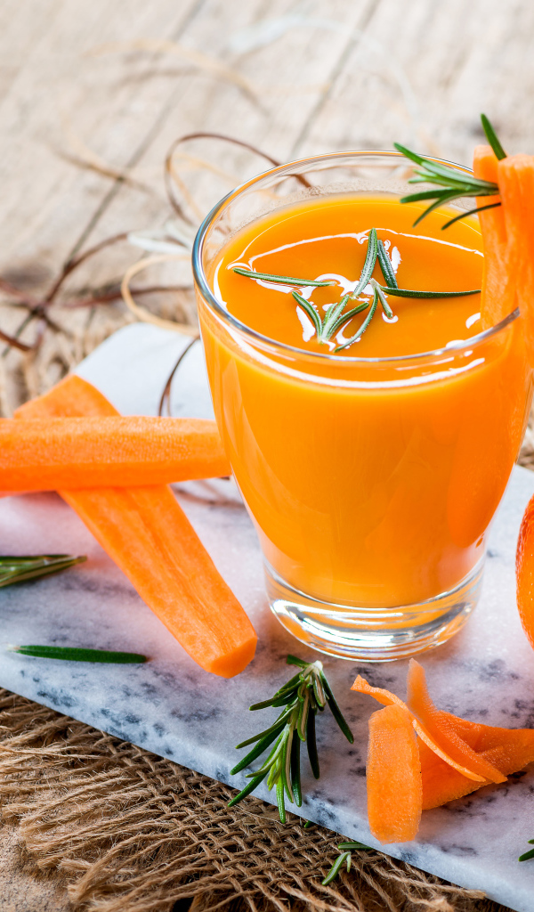 Два апельсина на столе со стаканом морковного сока