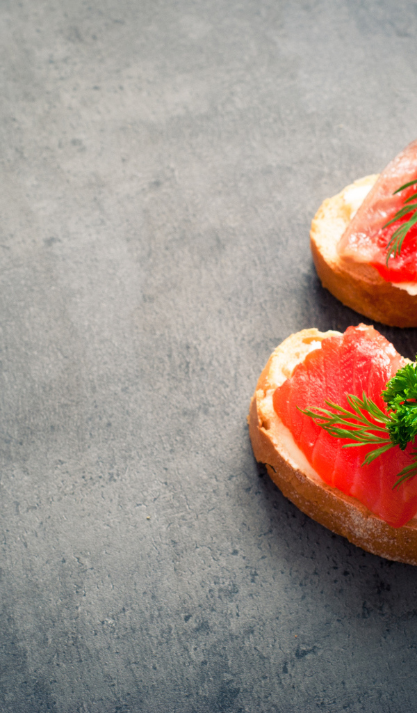 Два бутерброда с красной рыбой, огурцом и зеленью на черном фоне