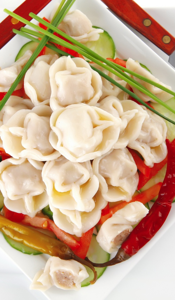 Белая тарелка с пельменями, красным перцем и огурцами