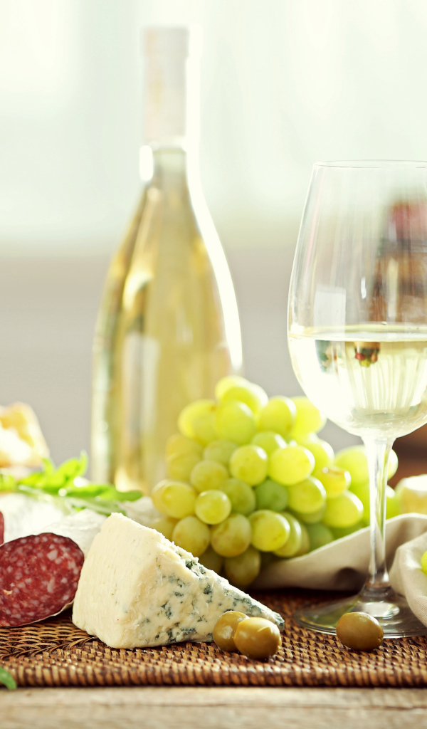 Белое вино на столе с сыром, колбасой и виноградом