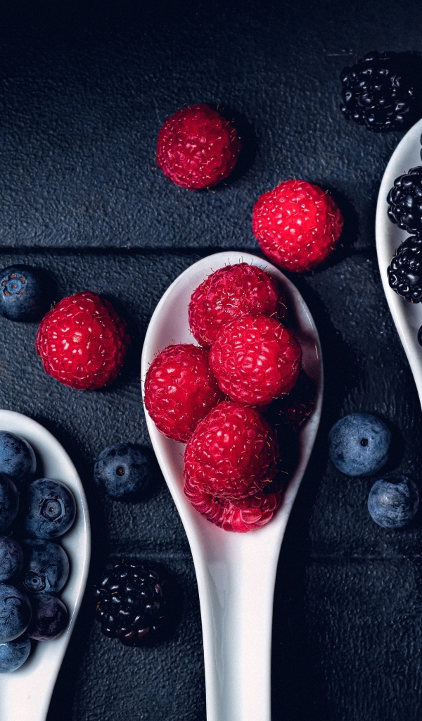 Ягоды черники, малины и ежевики на белых ложках