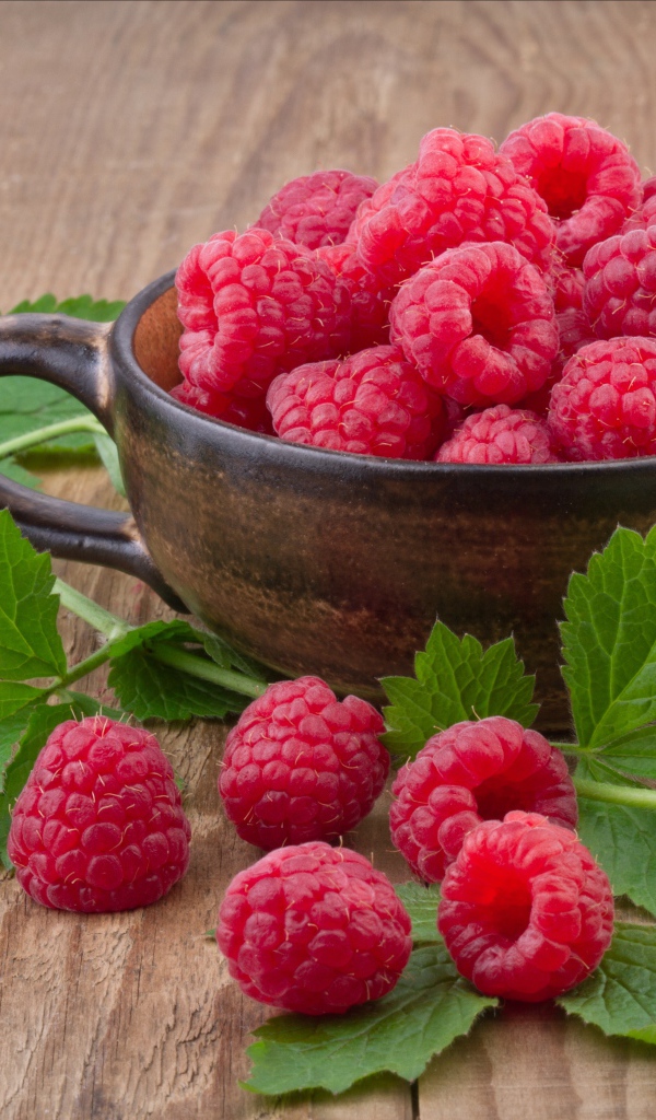 Чашка со свежей малиной на столе с зелеными листьями