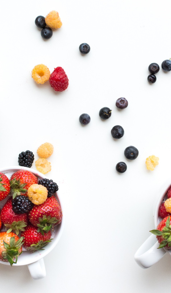 Чашки на столе с ягодами клубники, малины и ежевики 