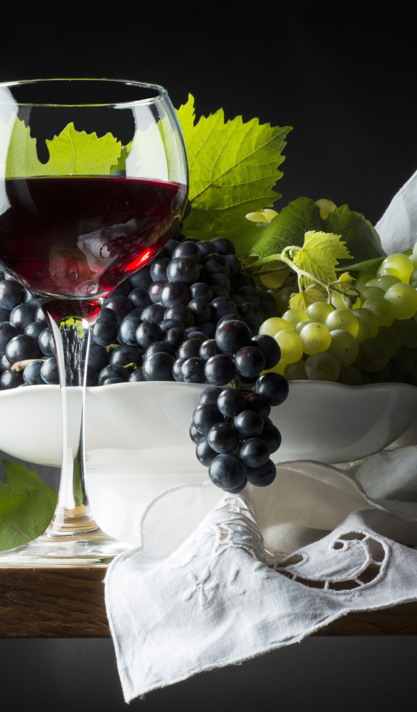 Бокал красного вина на столе с белым и синим виноградом