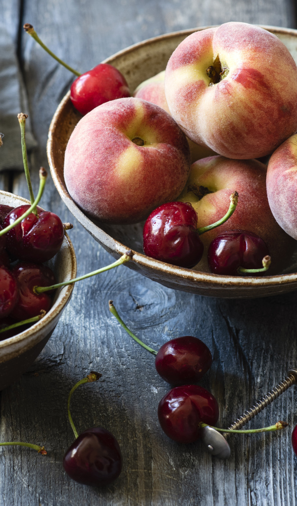 Спелые персики в миске на столе с черешней