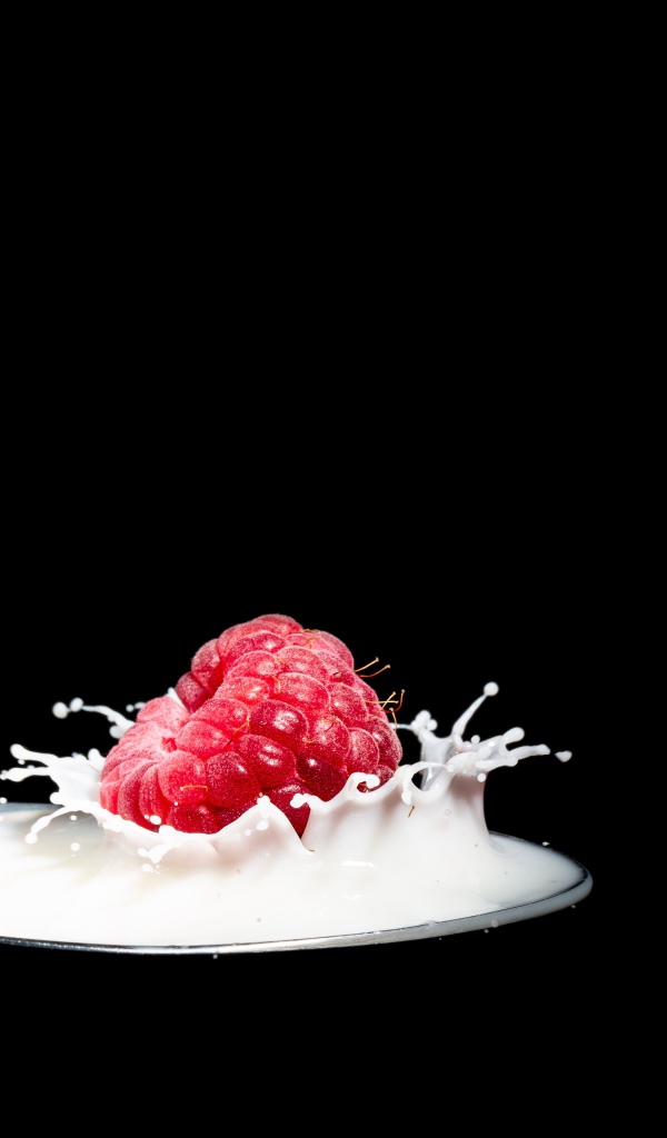 Спелая красная малина с ложке с молоком на черном фоне