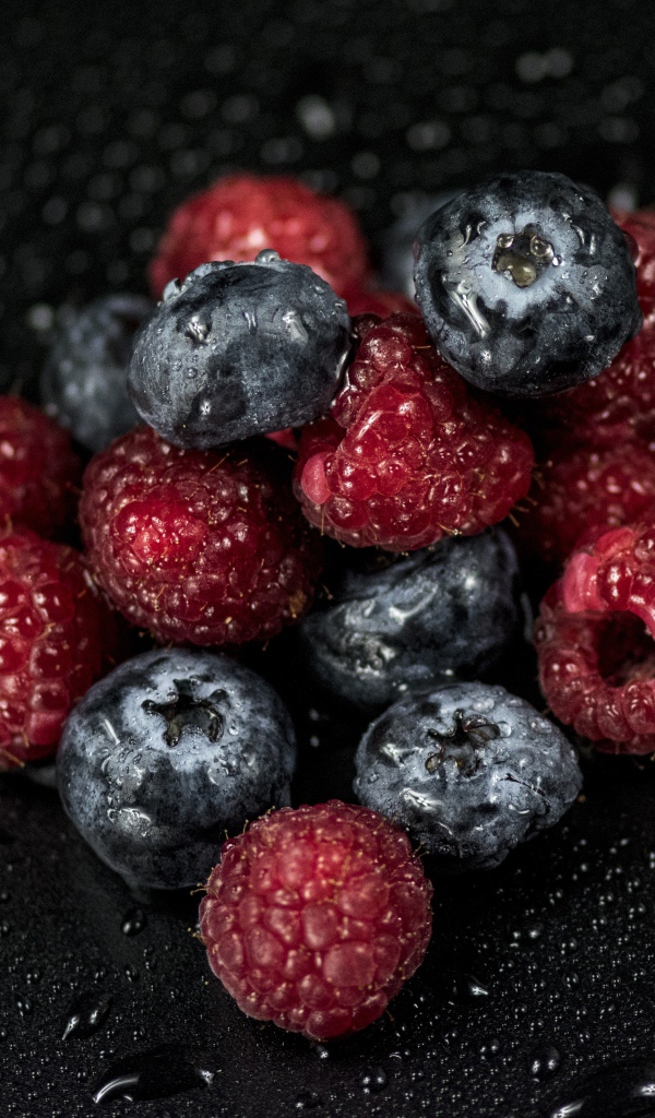 Мокрые ягоды черники и малины на черном фоне