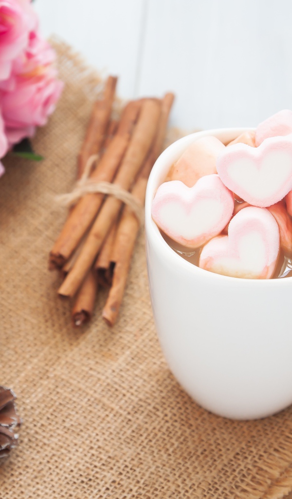 Чашка какао с маршмеллоу на столе с корицей, шишками и букетом розовых роз