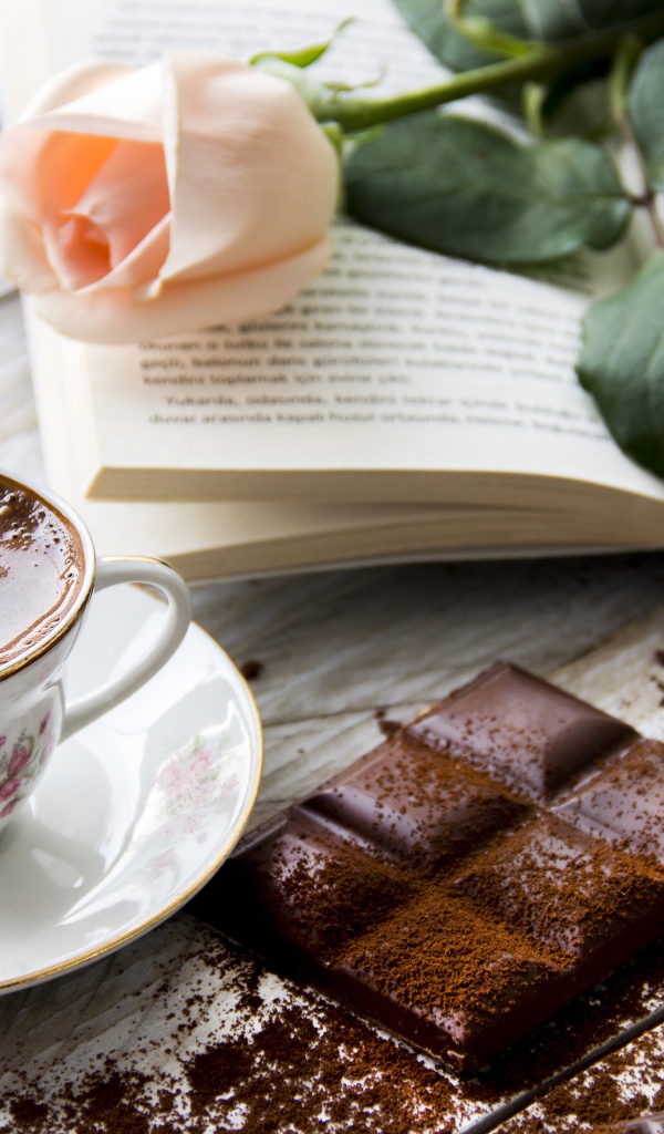 Чашка кофе на столе с шоколадом, книгой и розой