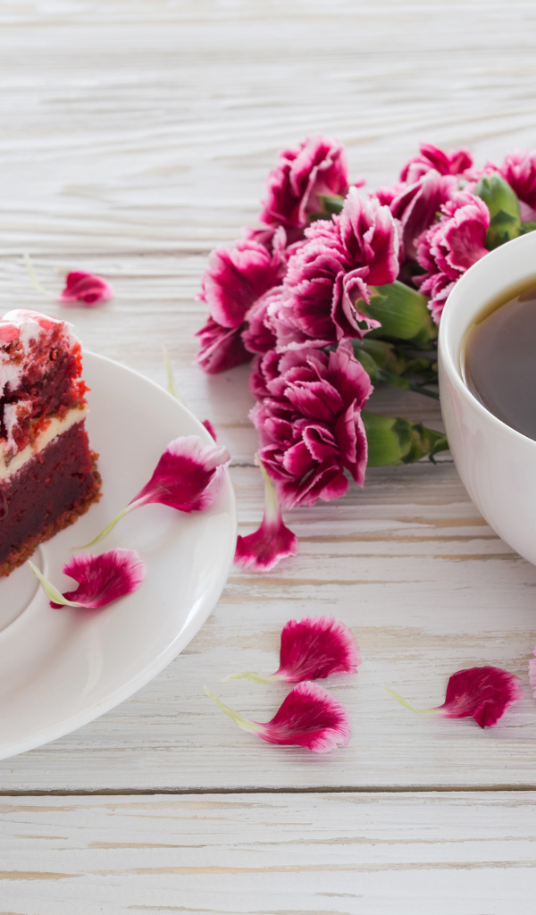Кусок торта на столе с букетом гвоздик и чашкой кофе