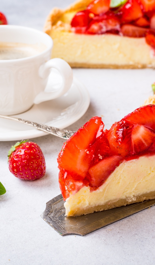 Кусок чизкейка с клубникой на столе с кофе