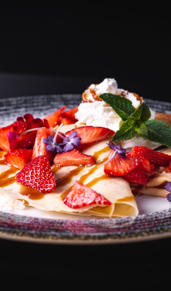 Аппетитные тонкие блинчики с клубникой на черном фоне