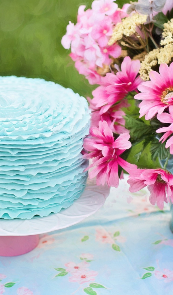Красивый торт с голубой глазурью на столе с букетом
