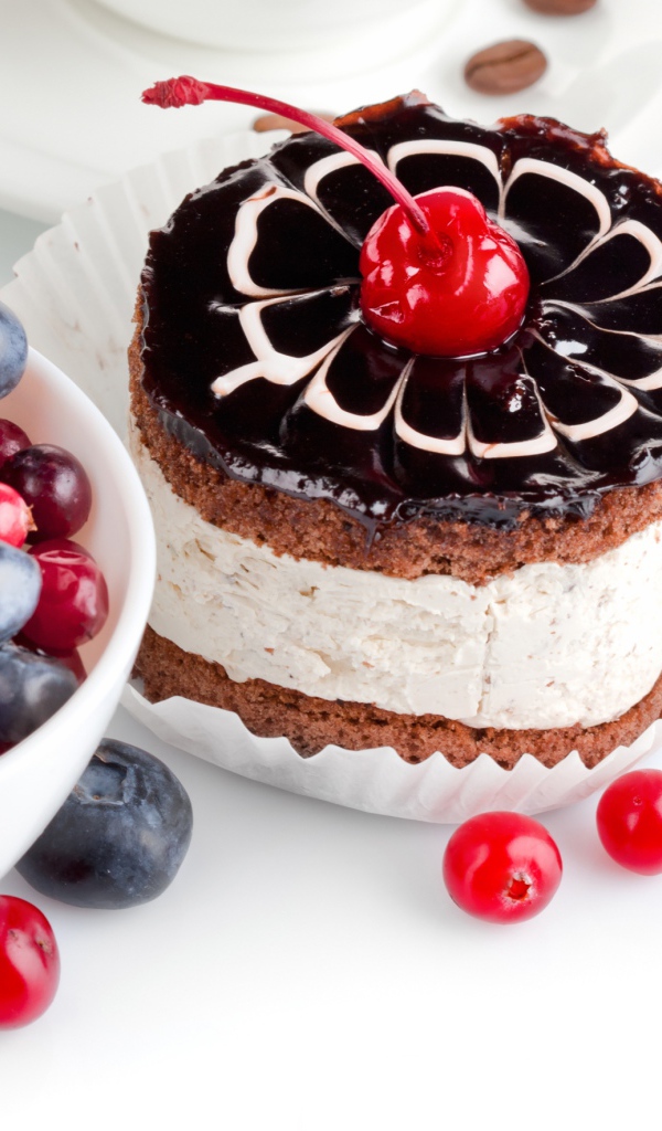 Пирожное с вишней на белом фоне с ягодами черники и клюквы