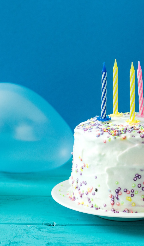 Праздничный торт со свечами, шариком и колпаком на голубом фоне