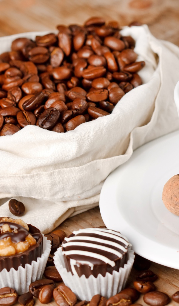 Шоколадные конфеты на столе с чашкой кофе и мешком с кофейными зернами