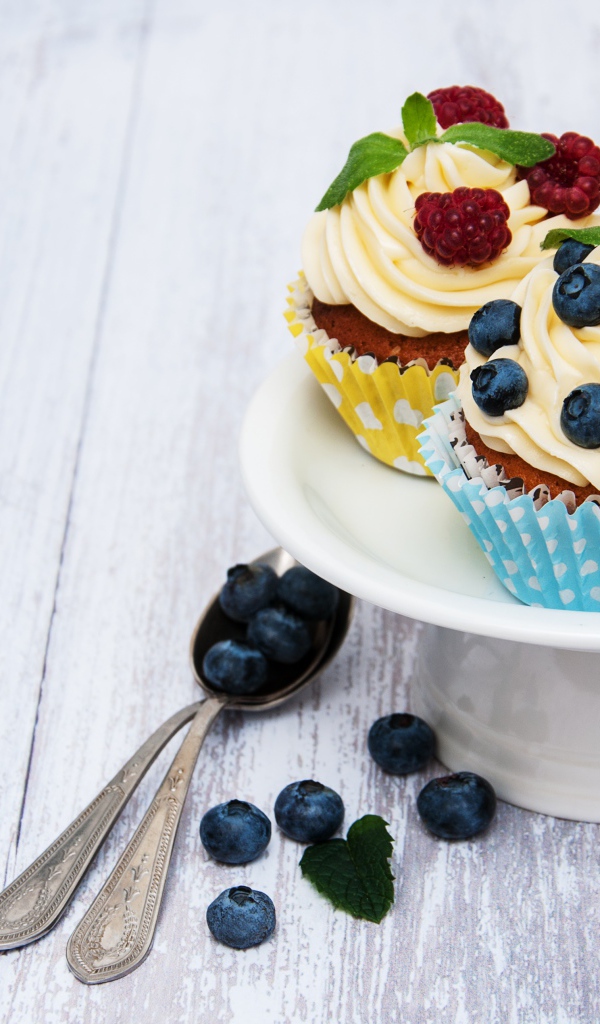 Кексы с кремом на белом блюде с ягодами