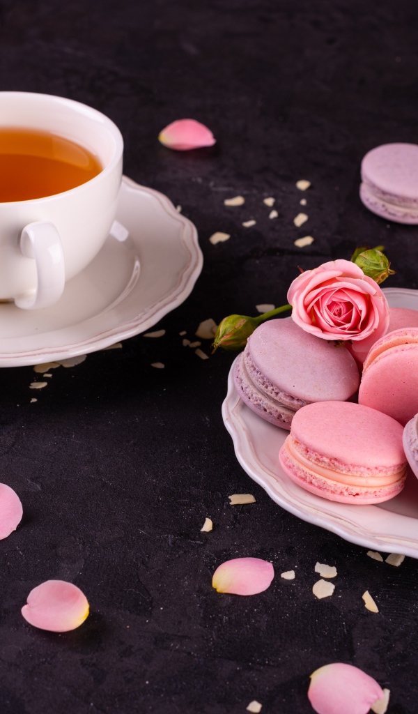 Нежный десерт макарон на столе с чашкой чая и розой